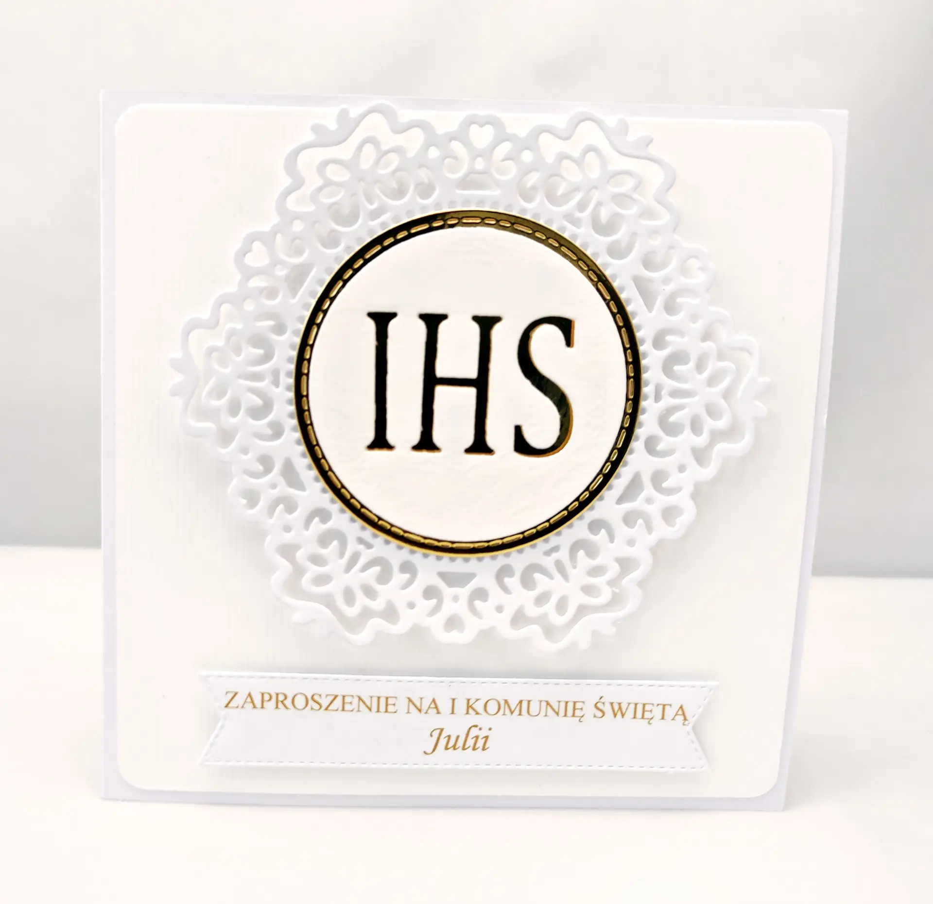 Ręcznie robione zaproszenie na Pierwszą Komunię Świętą, białe z koronkowym ornamentem i symbolem IHS na tle lustrzanego złota, eleganckie kwadratowe zaproszenie komunijne.