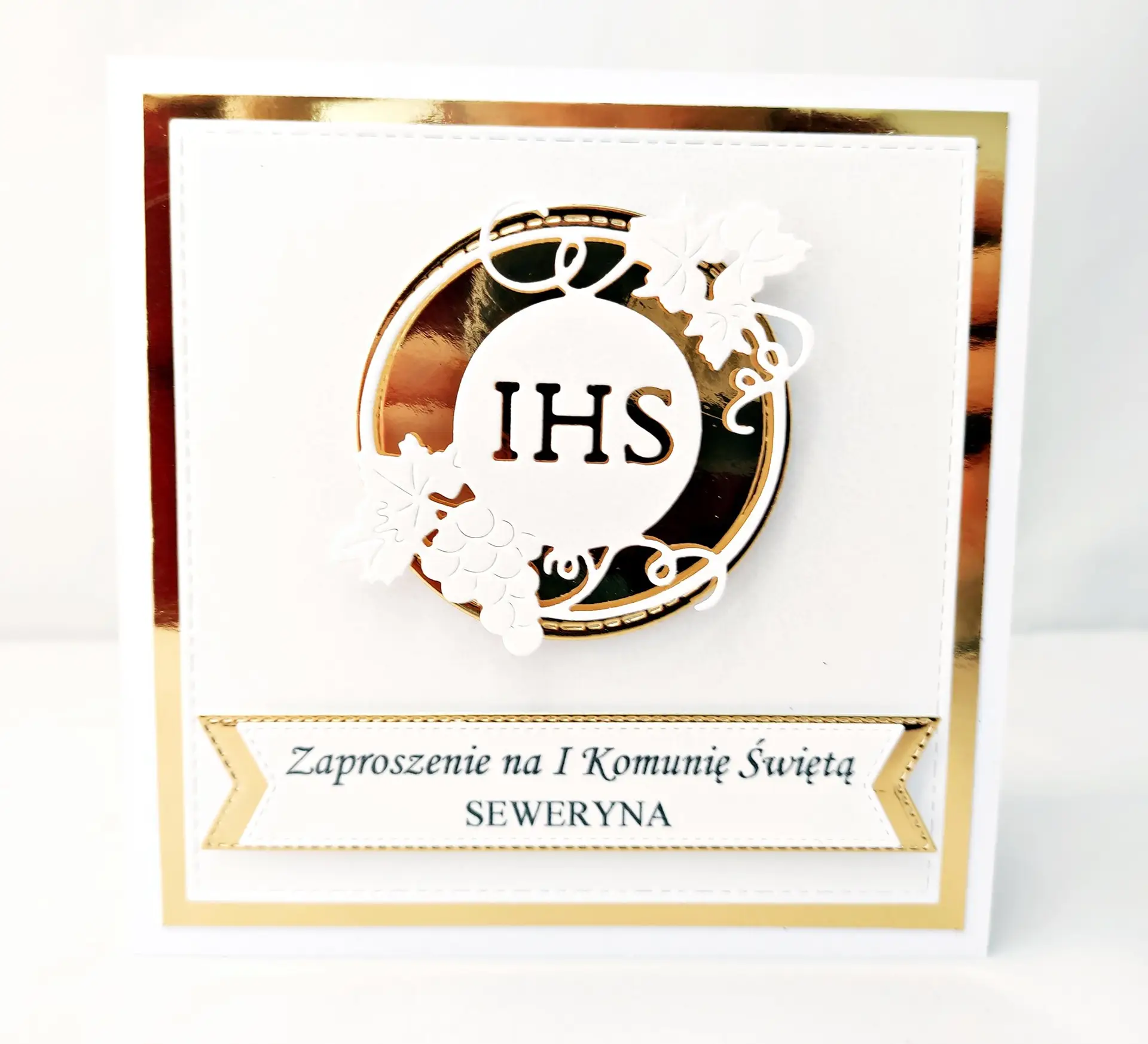 Ręcznie robione zaproszenie na Pierwszą Komunię Świętą z perłowej bieli, z motywem IHS w złotym okręgu na lustrzanym tle, eleganckie zaproszenie komunijne.