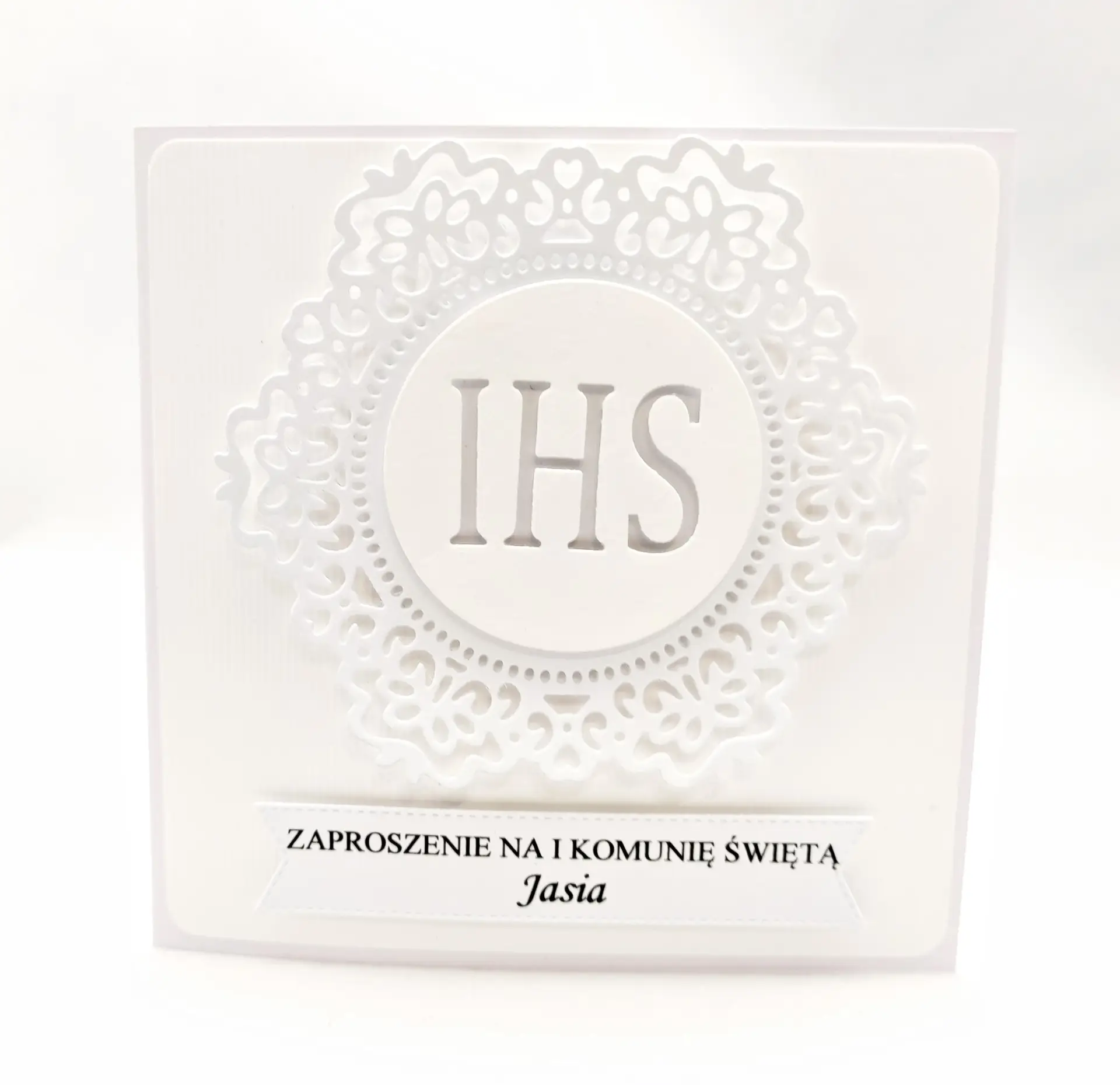 Białe zaproszenie na Pierwszą Komunię Świętą z koronkowym ornamentem i symbolem IHS, wykonane z papieru wizytówkowego, eleganckie kwadratowe zaproszenie w całości w bieli.
