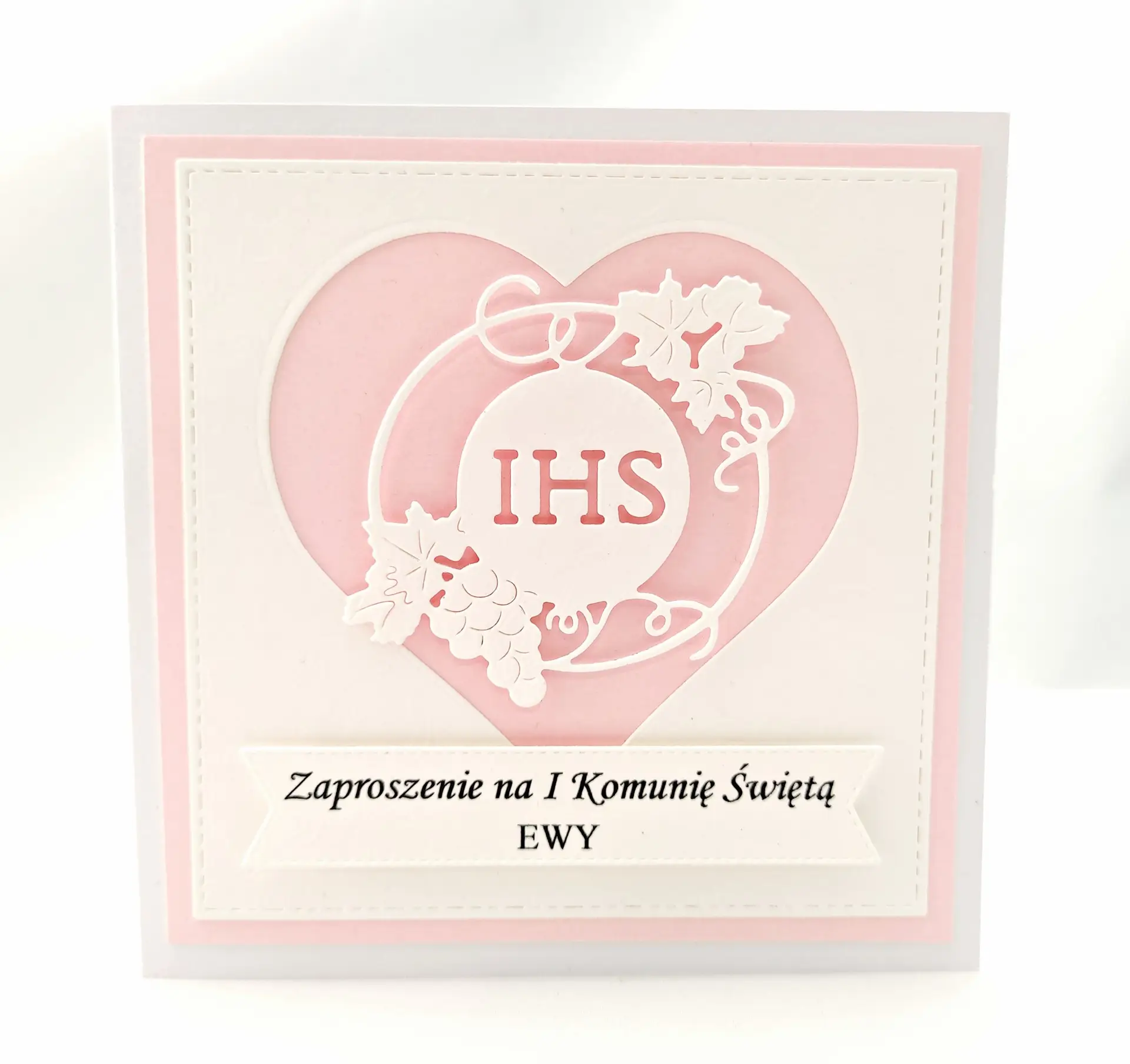 Zaproszenie na Pierwszą Komunię Świętą dla dziewczynki w kolorze różowym, z sercem i symbolem IHS, wykonane z papieru wizytówkowego, delikatne i dziewczęce zaproszenie komunijne.