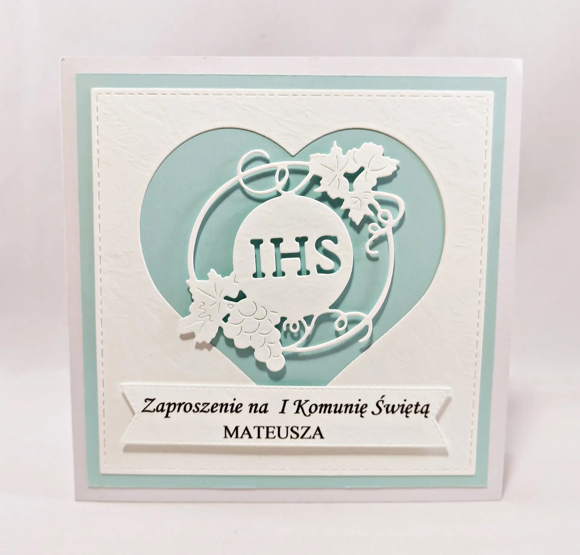 Błękitne zaproszenie na Pierwszą Komunię Świętą dla chłopca, z motywem serca i symbolem IHS, wykonane z papieru wizytówkowego, eleganckie i subtelne zaproszenie komunijne.