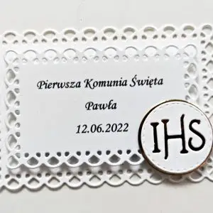 Ażurowa prostokątna etykieta na ciasto z symbolem IHS, zbliżenie na ręcznie wykonaną ramkę i elegancki nadruk na Pierwszą Komunię Świętą