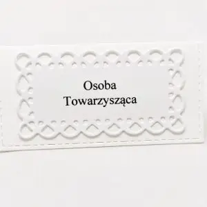 Biała winietka z ażurową ramką, wykonana z papieru wizytówkowego, ustawiona na stole, z miejscem na imię gościa
