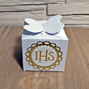 Ręcznie robione pudełeczko komunijne IHS z białego papieru i lustrzanego złota, widoczne z innej perspektywy, jako podziękowanie dla gości