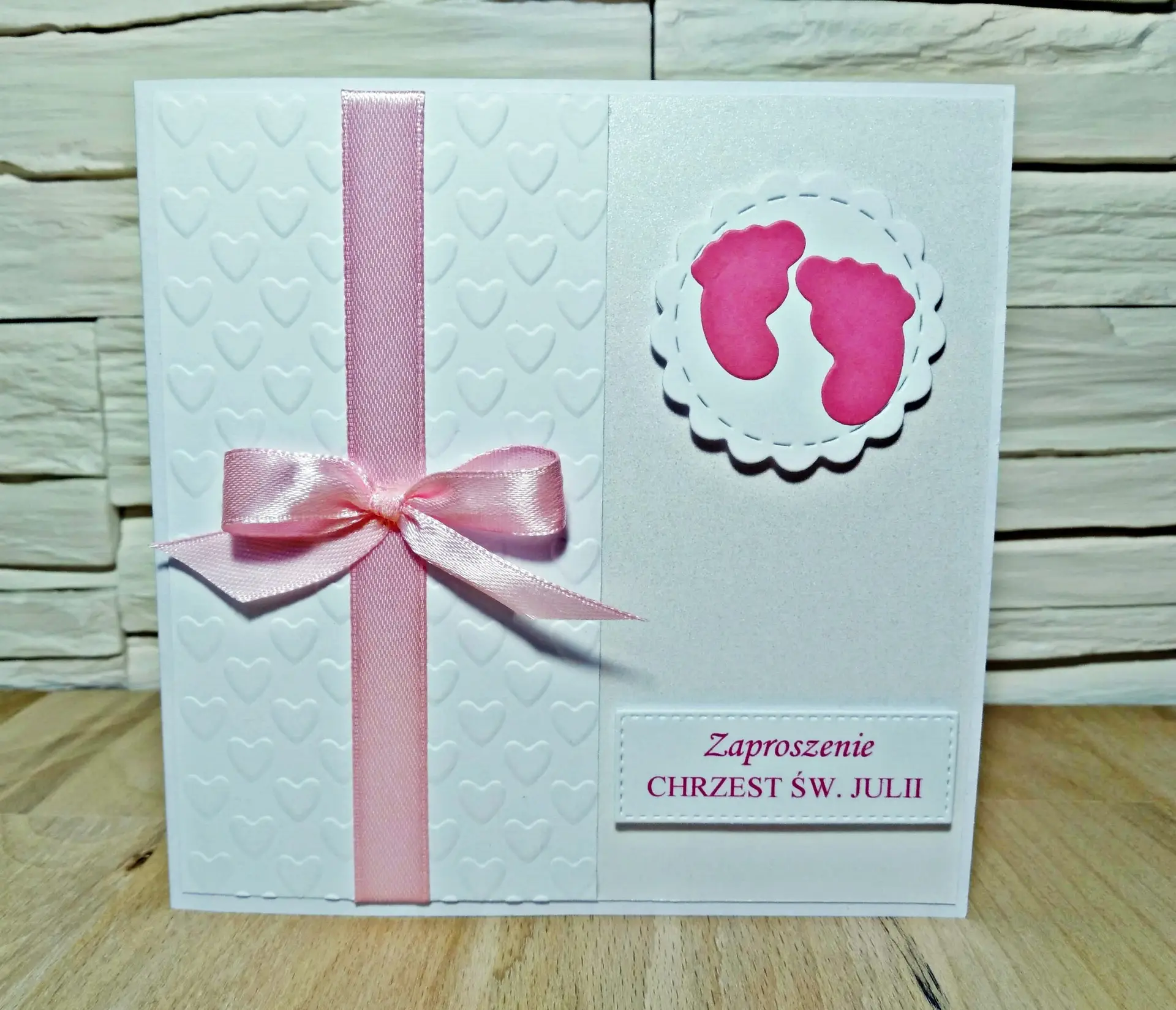 Zaproszenie na Chrzest Święty dziewczynki z motywem dziecięcych stópek, satynową wstążką, tłoczonym tłem w serduszka i różowymi detalami na perłowym papierze