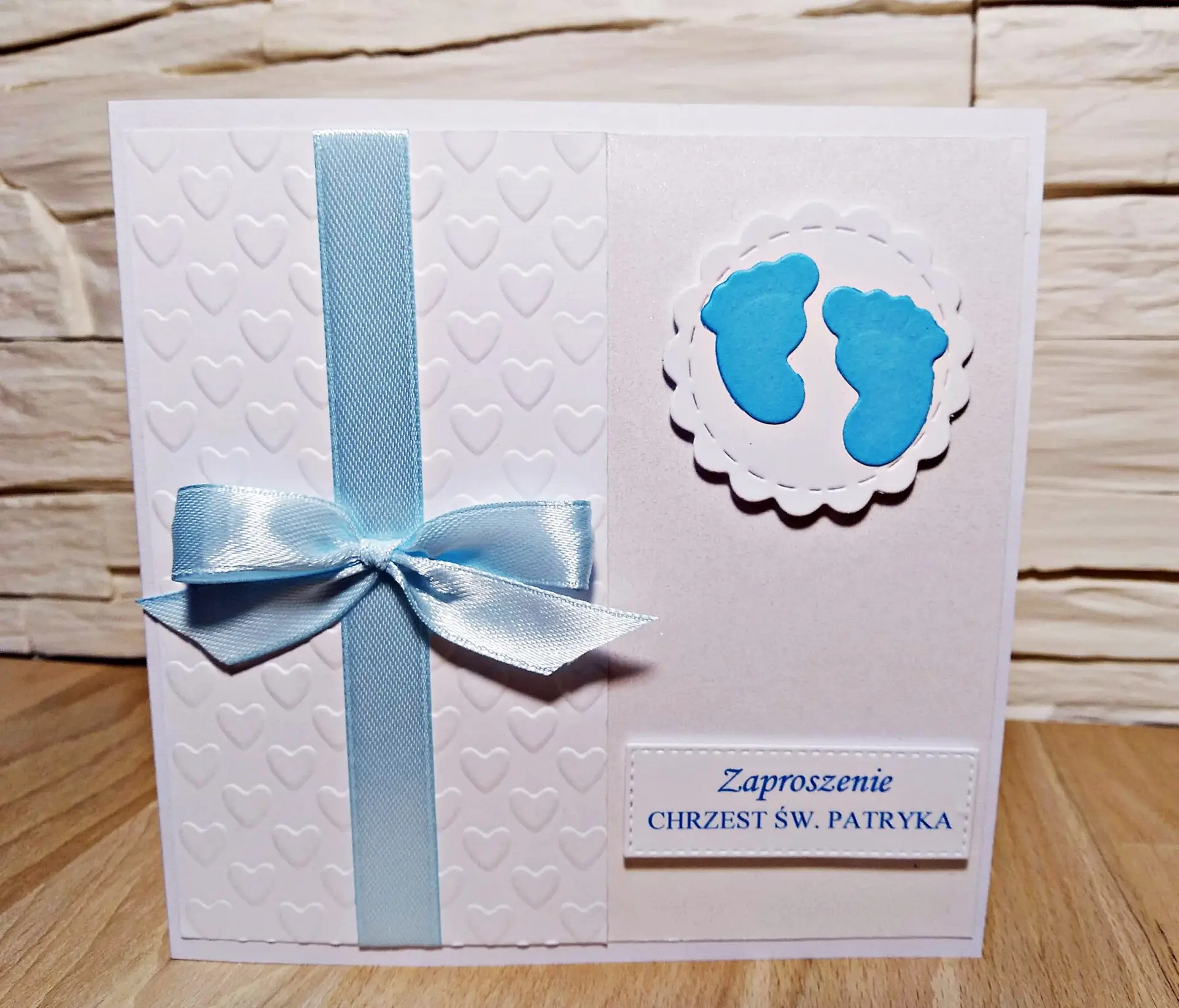 Zaproszenie na Chrzest Święty chłopca z motywem dziecięcych stópek, satynową wstążką, tłoczonym tłem w serduszka i błękitnymi detalami na perłowym papierze