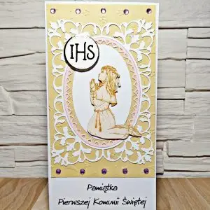 Ręcznie wykonana kartka komunijna DL z tekturową klęczącą dziewczynką w stroju komunijnym i napisem „Pamiątka Pierwszej Komunii Świętej”, subtelne komunijne zdobienia na dekoracyjnym tle
