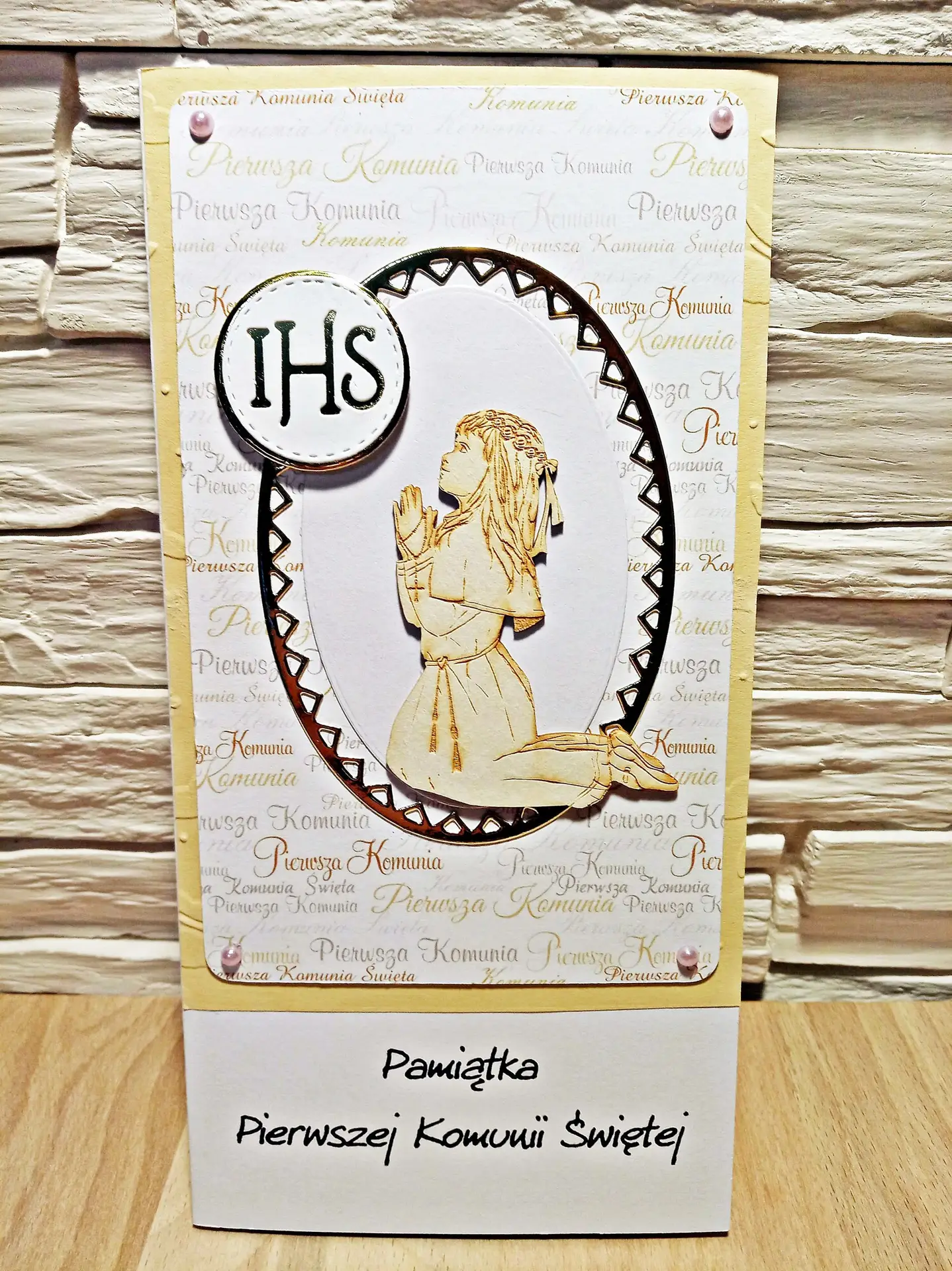 Kartka komunijna DL dla dziewczynki z tekturowym motywem klęczącej, modlącej się dziewczynki i napisem „Pamiątka Pierwszej Komunii Świętej”, eleganckie tło i delikatne zdobienia