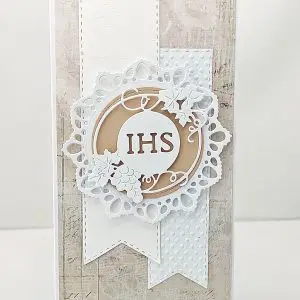 Elegancka kartka komunijna DL z centralnym motywem IHS na ozdobnym tle, delikatne tłoczenia i dekoracyjne elementy, ręcznie wykonana pamiątka Pierwszej Komunii Świętej