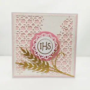 Ręcznie robiona kartka komunijna 13,5x13,5 dla dziewczynki, z motywem IHS i złotymi kłosami zbóż na ażurowym różowym tle, delikatna i elegancka pamiątka Pierwszej Komunii Świętej