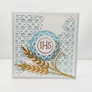 Kwadratowa kartka komunijna 13,5x13,5 dla chłopca, z motywem IHS i złotymi kłosami zbóż na ażurowym błękitnym tle, elegancka ręcznie robiona pamiątka Pierwszej Komunii Świętej