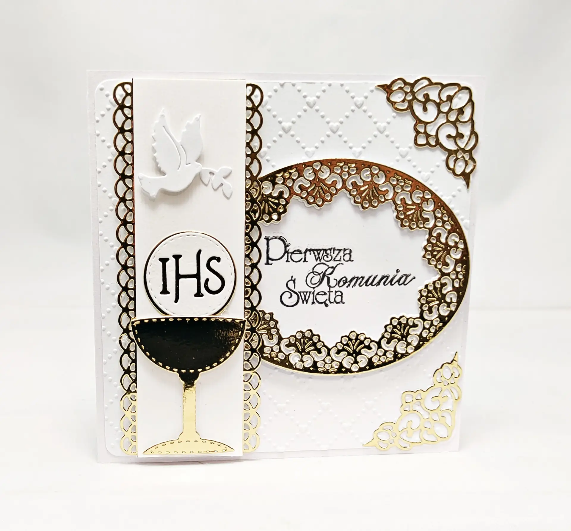 Ręcznie wykonana kartka komunijna w odcieniach bieli i złota, z motywem kielicha i napisem IHS, ozdobiona ażurowymi wycięciami i subtelnym połyskiem