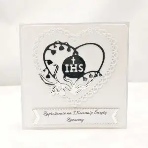 Biało-srebrne zaproszenie na Pierwszą Komunię Świętą z ażurowym sercem i sercem z konwalii wokół symbolu IHS, pojedyncze zaproszenie sfotografowane od frontu.