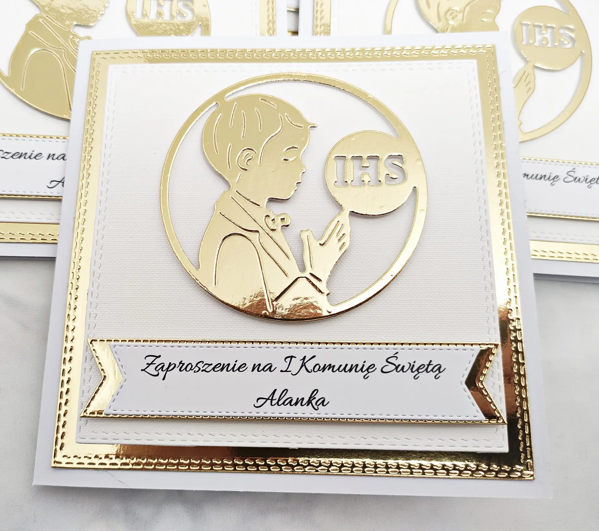 Zaproszenie na Pierwszą Komunię Świętą dla chłopca z sylwetką modlącego się chłopca i symbolem IHS, na białym papierze wizytówkowym z lustrzanym złotym tłem.