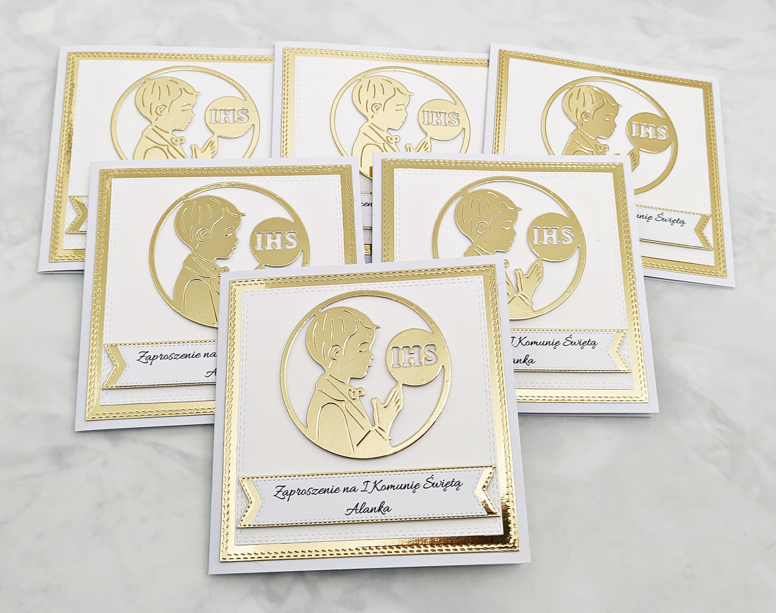 Zaproszenia komunijne dla chłopca z modlącym się chłopcem i symbolem IHS, na złotym tle, sfotografowane z góry w innej aranżacji, pokazujące serię kilku sztuk.
