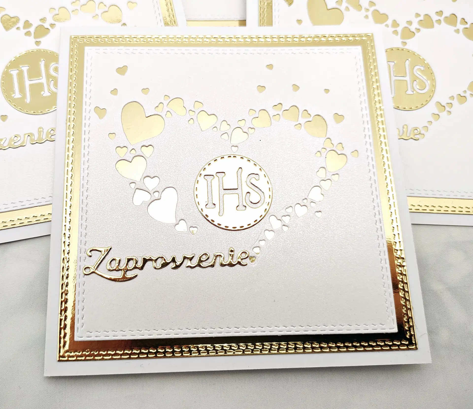 Pojedyncze zaproszenie na Pierwszą Komunię Świętą z sercem ułożonym z małych serduszek, symbolem IHS w środku i napisem „Zaproszenie” na białym tle.