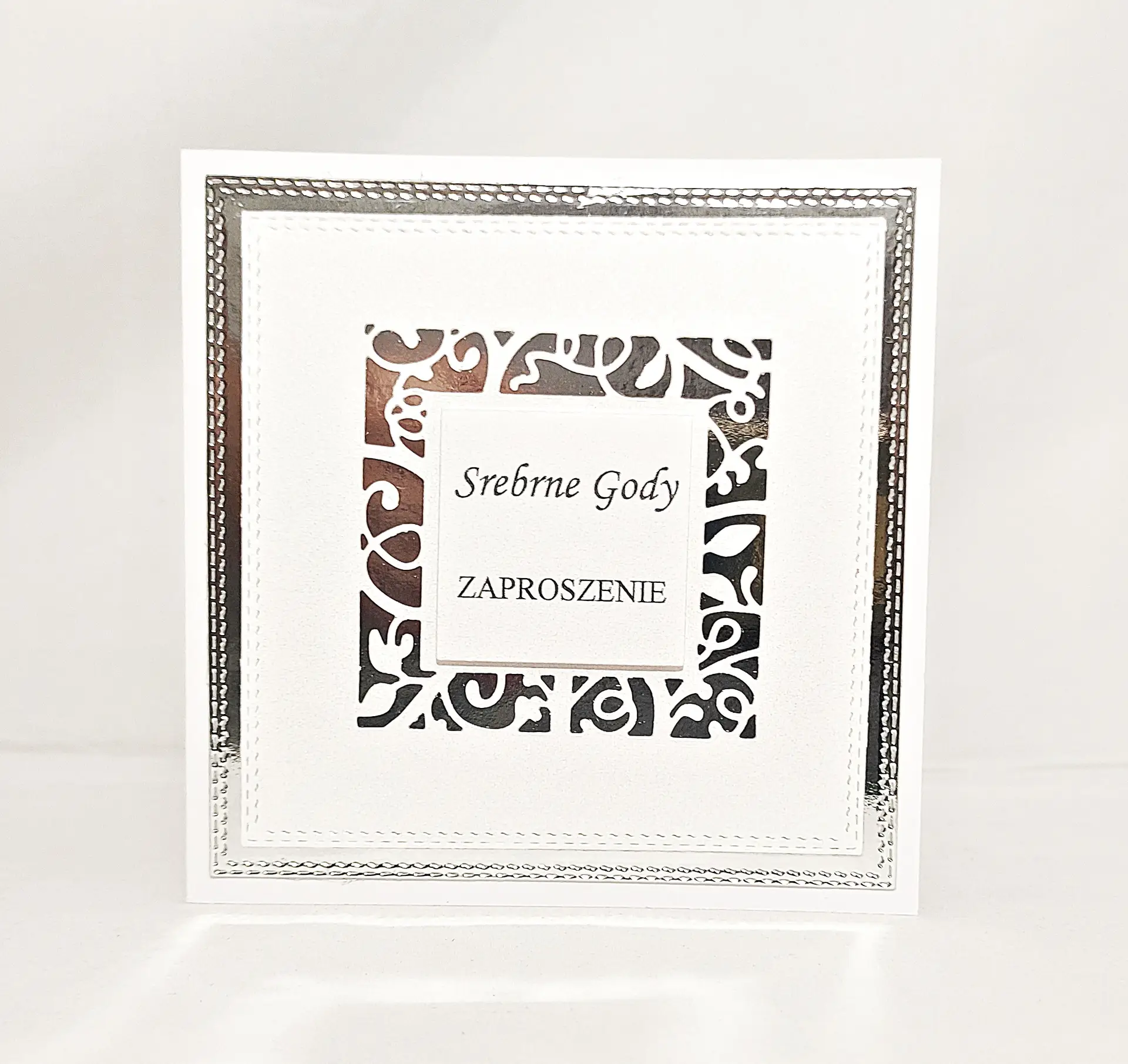 Eleganckie zaproszenie na 25 rocznicę ślubu Srebrne Gody na lustrzanym srebrnym tle, z białą ażurową ramką i napisem „Srebrne Gody – Zaproszenie” – widok od frontu